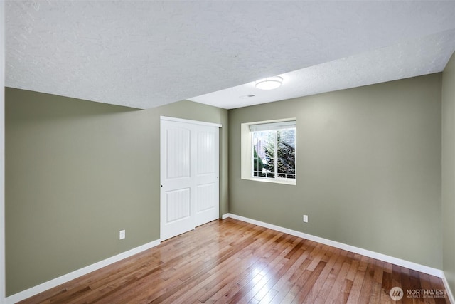 interior space with a closet, a textured ceiling, baseboards, and hardwood / wood-style flooring