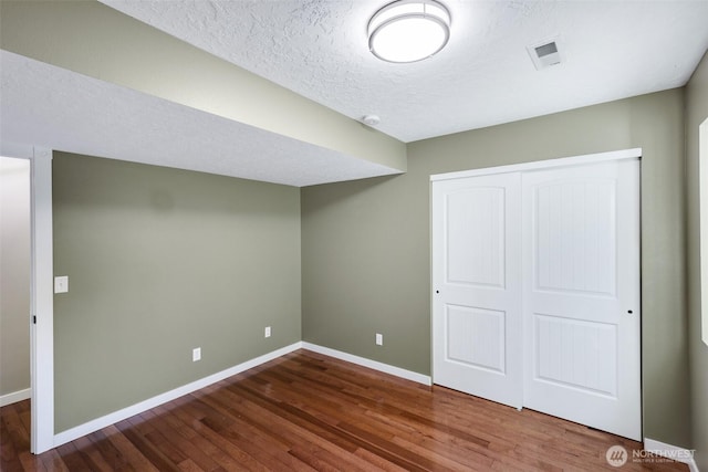 unfurnished bedroom featuring a closet, wood finished floors, visible vents, and baseboards