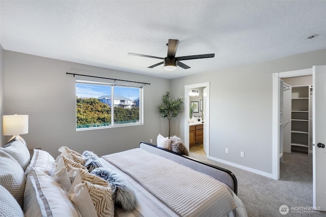 bedroom with light colored carpet, a spacious closet, a ceiling fan, a textured ceiling, and baseboards