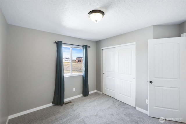 unfurnished bedroom featuring carpet, a textured ceiling, baseboards, and a closet