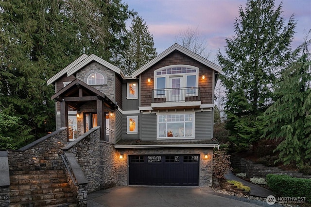 view of front of home featuring stone siding, driveway, a balcony, and an attached garage