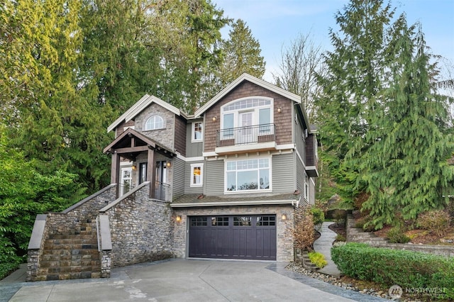 shingle-style home featuring stone siding, driveway, an attached garage, and a balcony