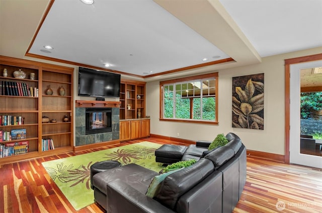 living room with a healthy amount of sunlight, a raised ceiling, a tiled fireplace, and wood finished floors