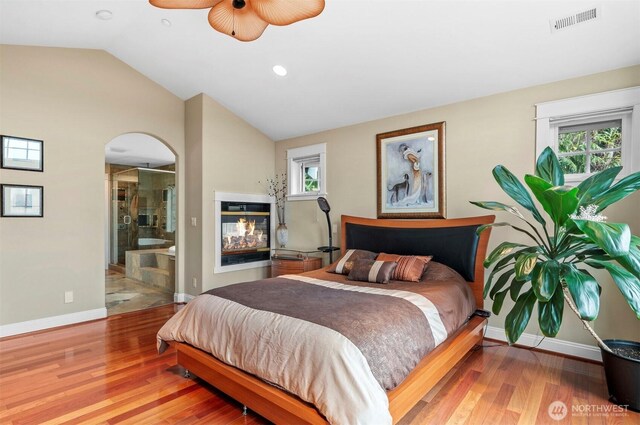 bedroom featuring lofted ceiling, wood finished floors, visible vents, and a multi sided fireplace