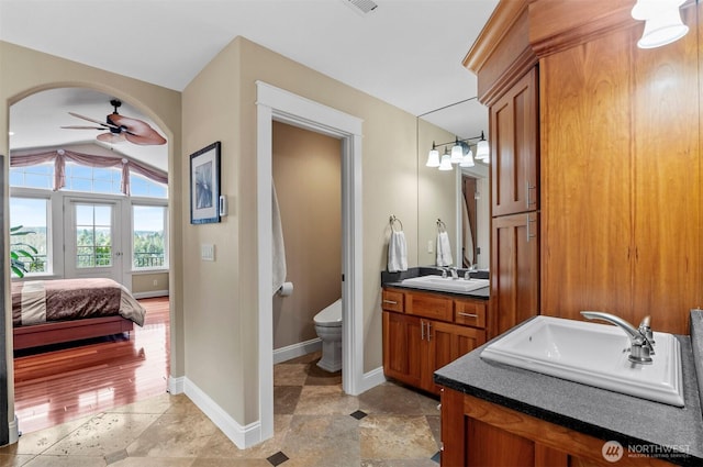 full bath featuring connected bathroom, toilet, vanity, baseboards, and a ceiling fan