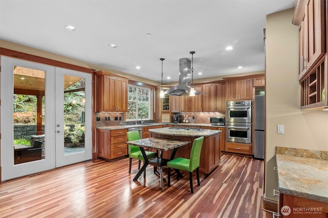 kitchen featuring island range hood, brown cabinetry, a kitchen island, appliances with stainless steel finishes, and wood finished floors