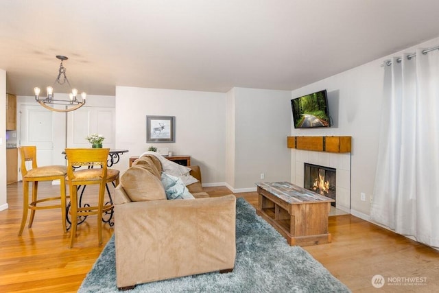 living room featuring a fireplace, light wood-style flooring, baseboards, and an inviting chandelier