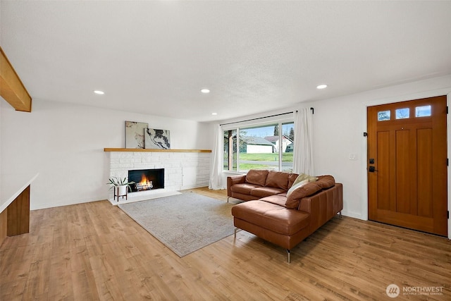 living area with light wood-style floors, a brick fireplace, and recessed lighting