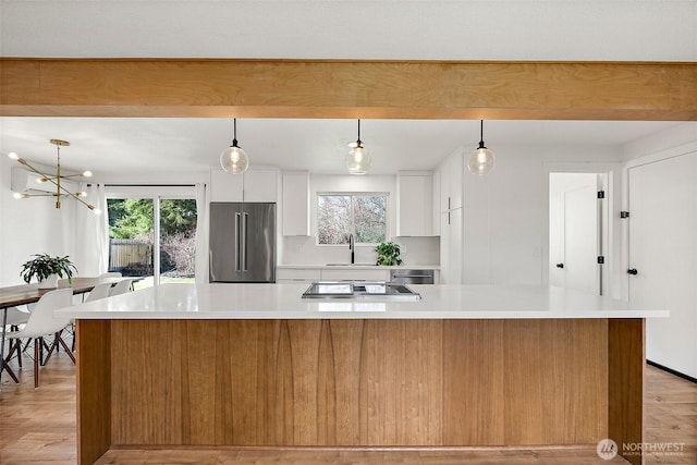 kitchen featuring high end fridge, light countertops, white cabinets, a sink, and black electric cooktop