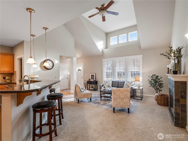 living room featuring light carpet, ceiling fan, a towering ceiling, and a tiled fireplace