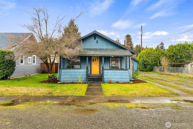 bungalow featuring a shingled roof, a chimney, fence, and a front yard