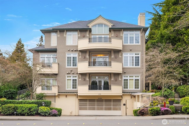 view of front of home with an attached garage, a balcony, and a chimney