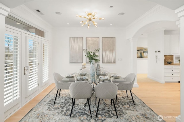 dining room with baseboards, visible vents, light wood finished floors, arched walkways, and ornamental molding