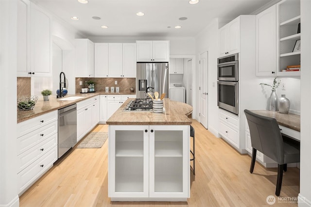 kitchen with a sink, a center island, appliances with stainless steel finishes, light stone countertops, and washer / dryer