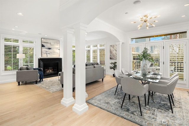 dining room with crown molding, a chandelier, light wood-type flooring, decorative columns, and a glass covered fireplace