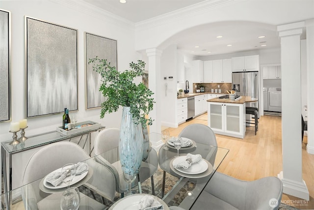 dining area featuring decorative columns, light wood-type flooring, ornamental molding, and washer and clothes dryer