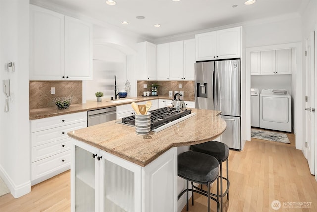 kitchen featuring light wood-type flooring, stainless steel appliances, separate washer and dryer, and a center island