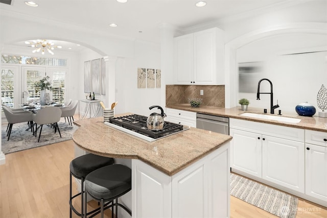 kitchen with a sink, a center island, gas stovetop, light wood finished floors, and dishwasher