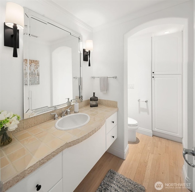 bathroom with vanity, wood finished floors, baseboards, ornamental molding, and toilet