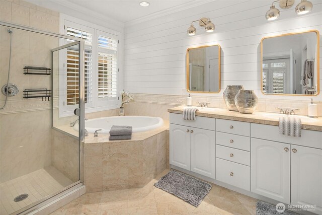 full bath with double vanity, a sink, a shower stall, crown molding, and a garden tub