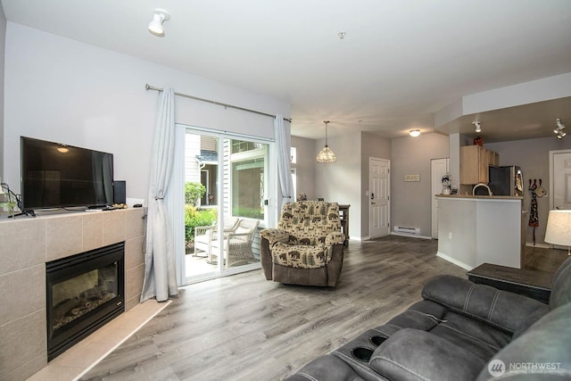 living room featuring a baseboard heating unit, a fireplace, baseboards, and light wood-style floors