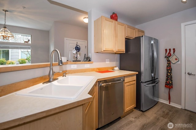 kitchen with appliances with stainless steel finishes, wood finished floors, light countertops, light brown cabinets, and a sink