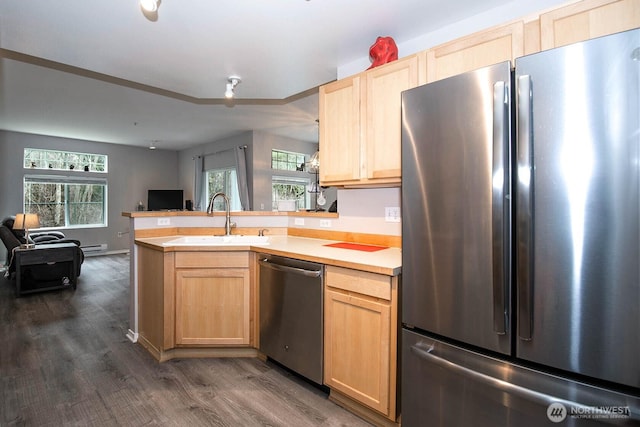 kitchen featuring appliances with stainless steel finishes, open floor plan, a sink, and light brown cabinetry