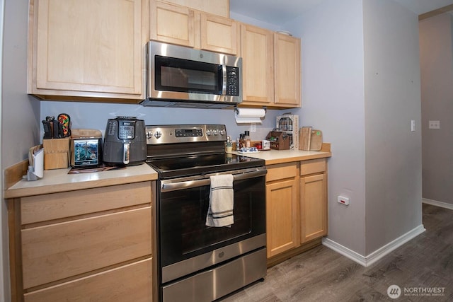 kitchen featuring light countertops, appliances with stainless steel finishes, light brown cabinets, wood finished floors, and baseboards