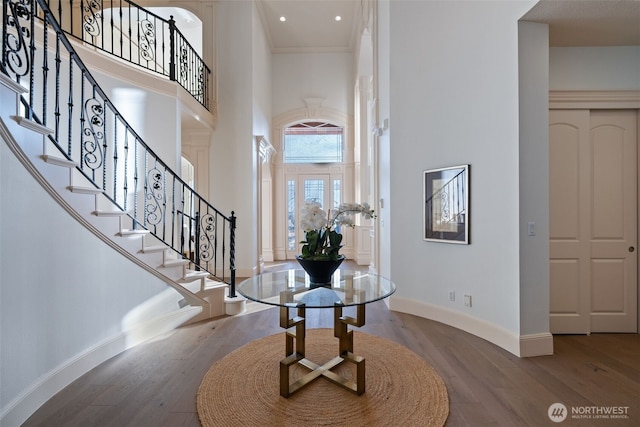 entrance foyer featuring a towering ceiling, stairway, baseboards, and wood finished floors