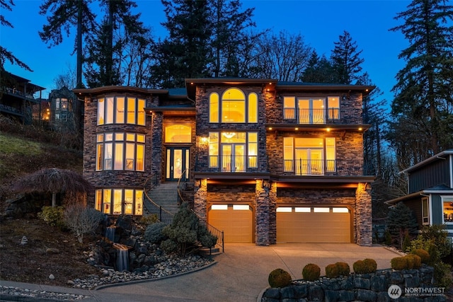 view of front facade with french doors, concrete driveway, an attached garage, a balcony, and stone siding