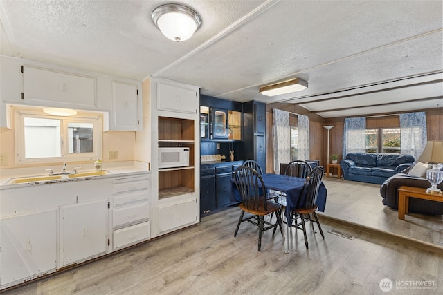 kitchen featuring white microwave, light wood finished floors, a sink, light countertops, and white cabinetry