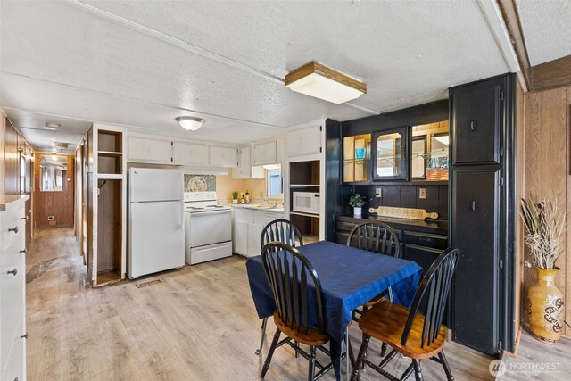 dining room featuring light wood-style flooring, wooden walls, and a textured ceiling