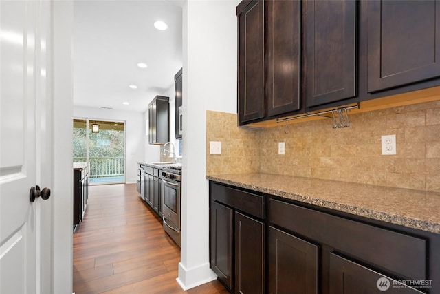 kitchen with dark wood-style floors, stainless steel range with gas cooktop, tasteful backsplash, dark brown cabinetry, and a sink