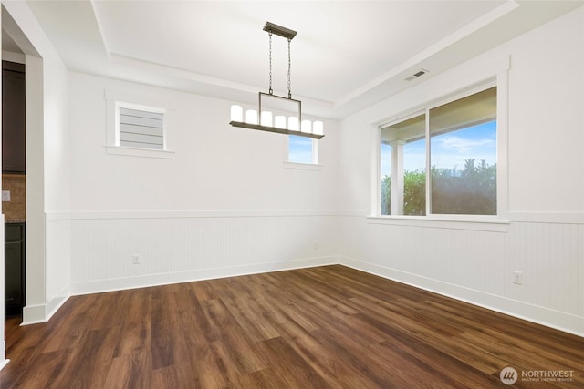 spare room with a tray ceiling, dark wood finished floors, and wainscoting