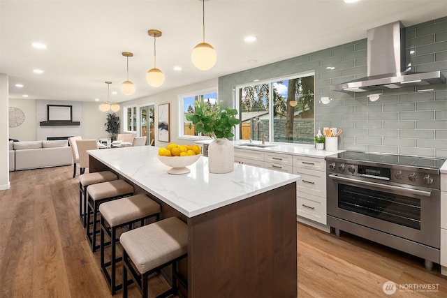 kitchen featuring tasteful backsplash, stainless steel range with electric cooktop, wall chimney range hood, white cabinetry, and a sink