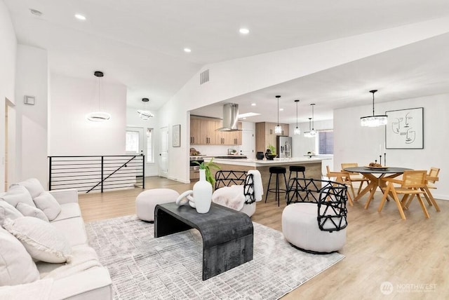 living area featuring visible vents, baseboards, light wood-style flooring, vaulted ceiling, and recessed lighting