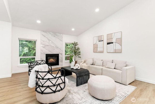 living room featuring baseboards, vaulted ceiling, light wood-type flooring, a fireplace, and recessed lighting