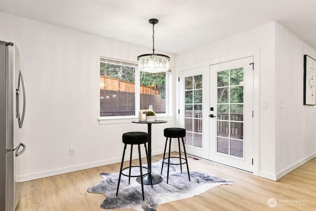 dining room featuring a chandelier, light wood-type flooring, french doors, and baseboards