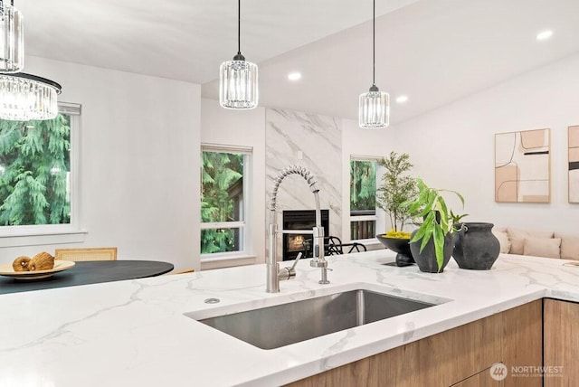 kitchen with brown cabinets, hanging light fixtures, light stone countertops, a sink, and recessed lighting