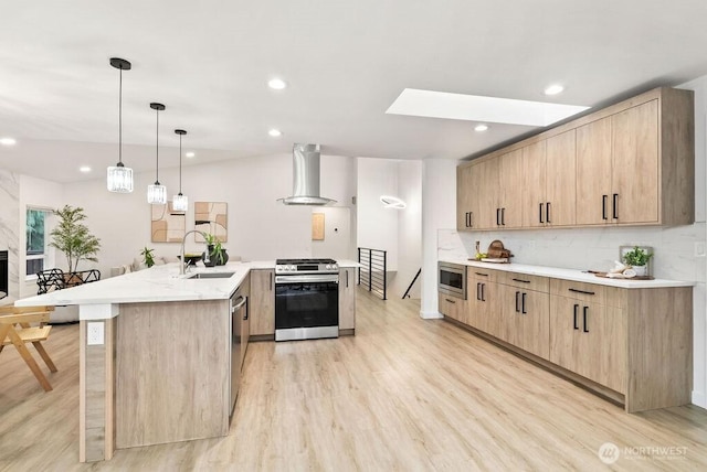 kitchen featuring light brown cabinets, wall chimney range hood, appliances with stainless steel finishes, and a sink