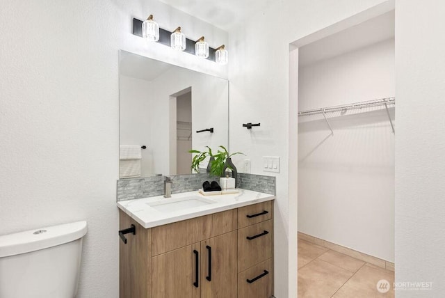 bathroom featuring a walk in closet, backsplash, toilet, vanity, and tile patterned flooring