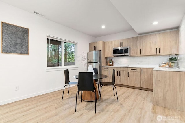 kitchen featuring light wood-style flooring, stainless steel appliances, light countertops, light brown cabinets, and backsplash