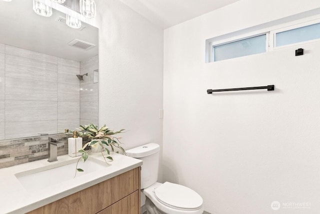 bathroom with visible vents, decorative backsplash, tiled shower, toilet, and vanity