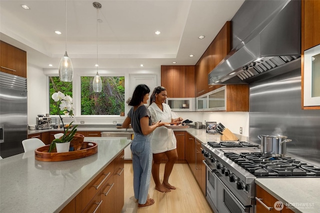 1514 Alki Ave SW, Seattle, WA 98116 - kitchen with wall chimney exhaust hood, high quality appliances, brown cabinets, light wood-style floors, and glass insert cabinets