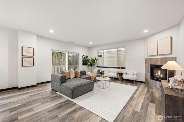 living room featuring light wood-type flooring, a fireplace, baseboards, and recessed lighting