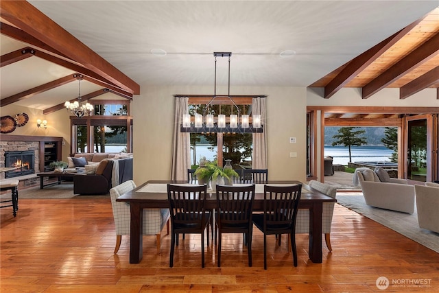 dining area featuring a chandelier, wood-type flooring, a fireplace, and lofted ceiling with beams