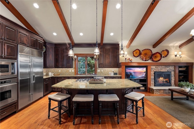 kitchen with built in appliances, a fireplace, a kitchen island, a kitchen breakfast bar, and light stone countertops