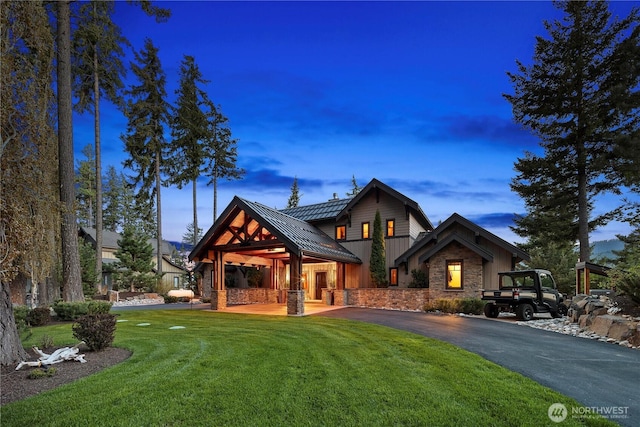 view of front of property with driveway, stone siding, metal roof, a standing seam roof, and a yard