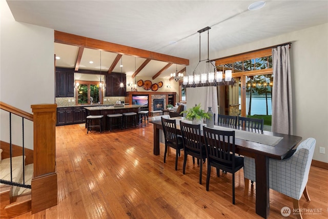 dining room with light wood-style flooring, beamed ceiling, an inviting chandelier, stairs, and a fireplace