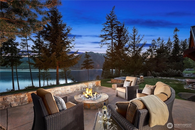 patio terrace at dusk featuring fence, a water and mountain view, and an outdoor living space with a fire pit